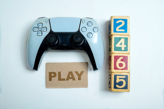 Modern white and black wireless gaming controller with a greeting card of Play and wooden cubes of numbers on a white background