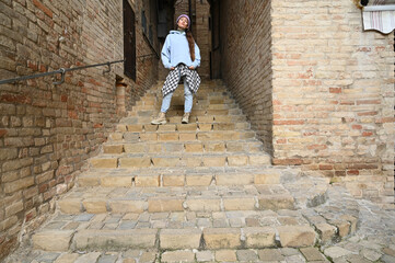 Middle-aged man dressed in a shirt and tie confidently descends the stone stairs between rustic brick walls, exuding charm and style in a timeless Italian setting.
