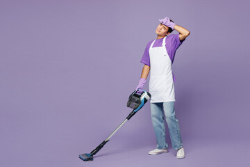 Full body young tired exhausted man wear violet t-shirt cleaning room using modern vacuum cleaner while doing housework tidy up isolated on plain pastel light purple background. Housekeeping concept.