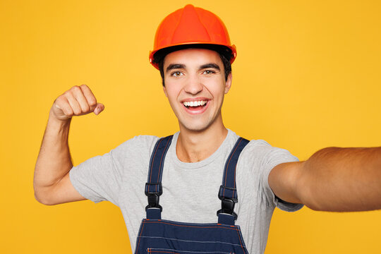 Young employee laborer handyman man he wear helmet overall do mobile cell phone selfie shot isolated on plain yellow background. Instruments accessories renovation apartment room. Repair home concept.