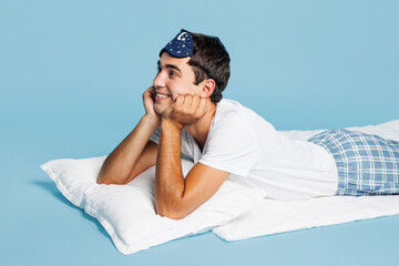 Obraz premium Side profile view calm dreamful minded young man he wears pyjamas jam sleep eye mask rest relax at home lying on bed isolated on plain pastel light blue cyan background. Good mood night nap concept.