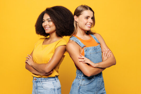 Side profile view two young friends buddies women they wear denim casual clothes hold hands crossed folded together smile isolated on plain yellow orange background studio portrait. Lifestyle concept. - Powered by Adobe
