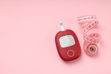 Blood glucose monitor beside measuring tape on pink background