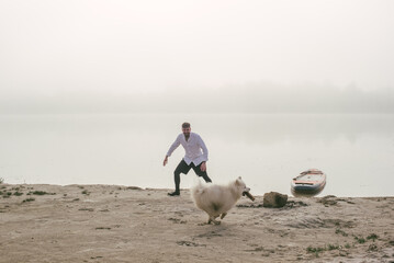 man playing with his cute samoyed dog at the lake during sunset