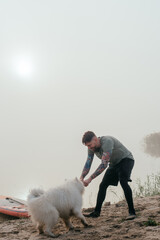 man playing with his cute samoyed dog at the lake during sunset