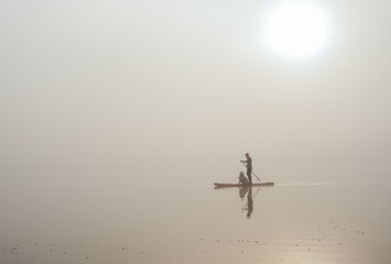 young man with tattooed arms on a sup board with his samoyed dog at the lake during sunset