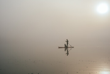 young man with tattooed arms on a sup board with his samoyed dog at the lake during sunset