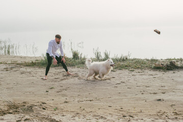man playing with his cute samoyed dog at the lake during sunset