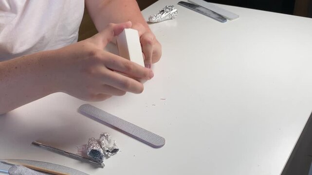 woman using soft nail buffer to gently polish and smooth the surface of her natural nails during manicure procedure in beauty salon