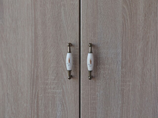 Wooden cabinet doors with decorative handles, close-up shot of the details. The cabinet doors are made of wood with a light brown color, and the handles are white with a floral design