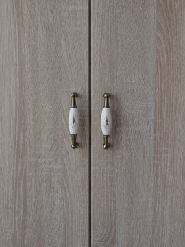 Close-up of a wooden cabinet with decorative white and gold handles. The cabinet doors are closed, and the handles are the focal point of the image, adding a touch of elegance
