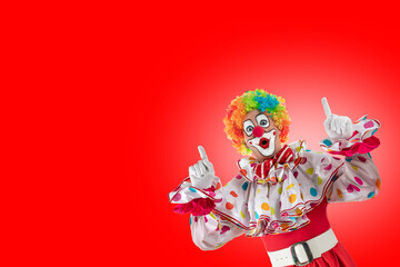 Funny clown pointing up at blank template copy spase for advertising, posters, greetings, invitations. Entertainer as Joker in a suit and wig, with clown whiteface makeup