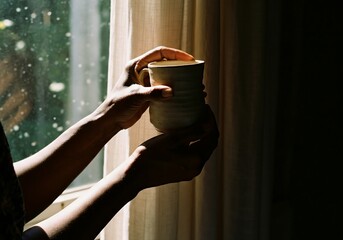 Hands holding ceramic mug near window light