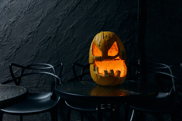A scary Halloween pumpkin head glows from within on the table.