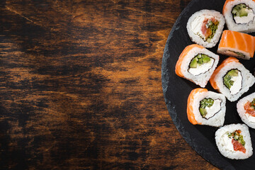 Philadelphia sushi roll salmon on round slate board and textured wooden surface with soft shadows.