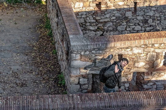 View from Torre del Llamp in Girona showing a tourist in a black jacket and jeans waving while walking through sunlit ancient stone passageways. Girona, Spain