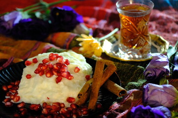 Ramadan dessert: Güllaç. Topped with pomegranate and cinnamon sticks. Tea in a crystal glass. Silver tea saucer. Purple roses and yellow daisies. Iftar table. Turkish milk desserts.
