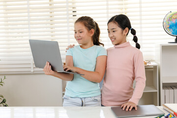 girls are standing, smiling, and looking intently at a laptop screen together, indicating joyful and friendly collaboration or learning in the digital age.