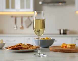 Elegant flute glass of white wine served with an assortment of crackers and chips on a marble kitchen counter in a modern home.
