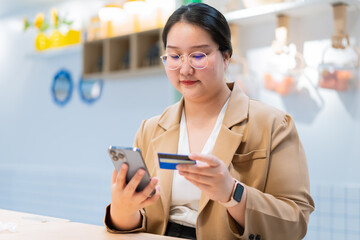 Young woman holding credit card and smartphone, online shopping or mobile banking concept, casual business attire, indoor modern setting, focused expression
