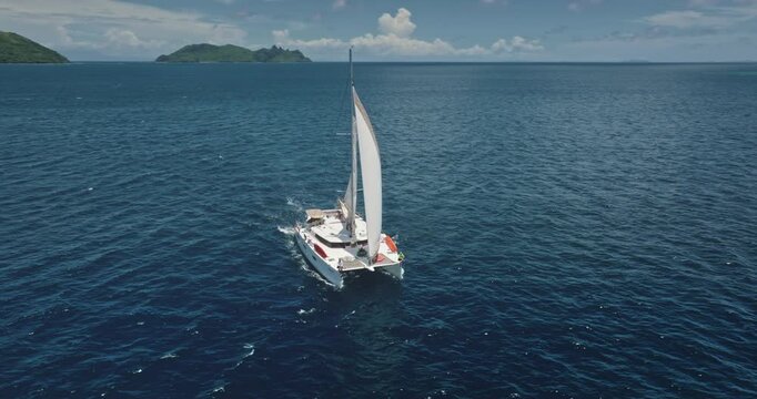 Catamaran sailing in the ocean near Kuata island, Fiji, aerial drone footage capturing the vastness of the sea and the beauty of the tropical islands in the background. Drone flight footage