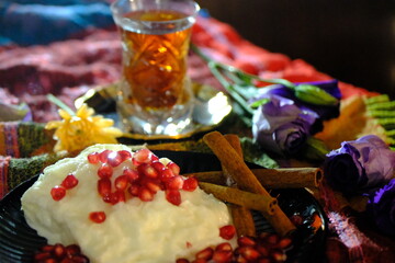 Ramadan dessert: Güllaç. Topped with pomegranate and cinnamon sticks. Tea in a crystal glass. Silver tea saucer. Purple roses and yellow daisies. Iftar table. Turkish milk desserts.
