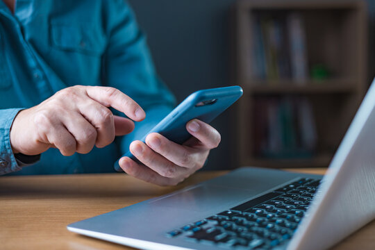 Dual technology work and communication concept, man's hands using smartphone while working on laptop at desk. Online business, multitasking, digital connection, modern professional workspace.