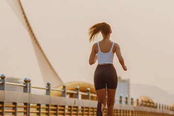 Young caucasian female running on sunny bridge in sportswear