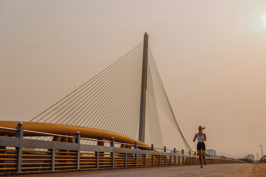 Female runner on bridge at sunset with modern architecture and cable design