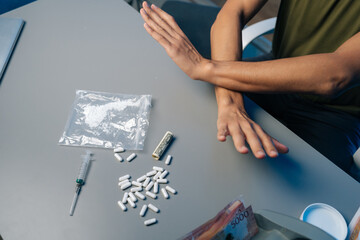 Recovering drug user pushing away narcotics, surrounded by scattered medical tools and...
