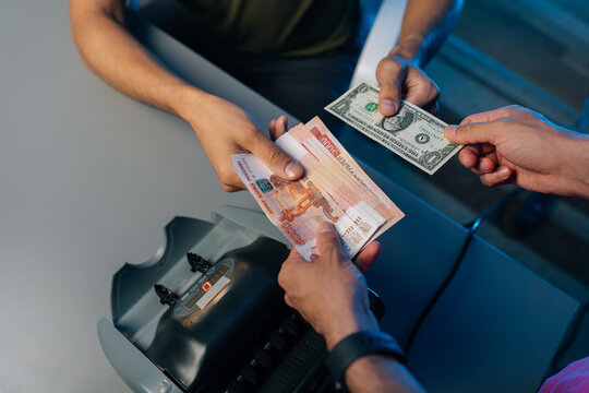 Close-up cropped shot of unrecognizable bank employees or cashiers exchanging Russian rubles and us dollars at exchange office, using money counting machine to ensure accuracy in transaction.