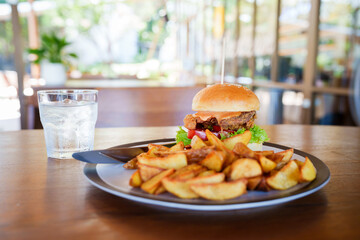 A woman is sitting at a restaurant table enjoying a delicious fried chicken burger with potato...