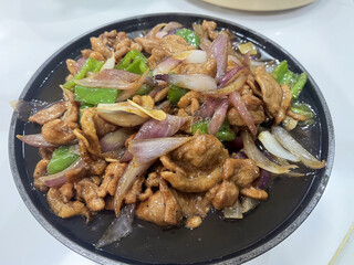 Stir fried chicken with sliced red onion and green pepper in savory sauce, sizzling presentation with glossy glaze and appetizing aroma