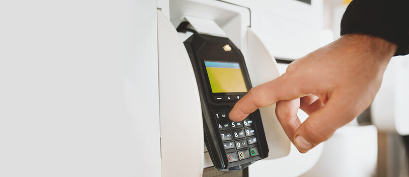 Customer entering PIN code on payment terminal at self-service kiosk in modern store or restaurant, making electronic transaction using debit or credit card machine banner copy space