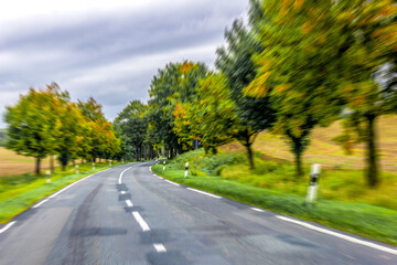 Curved asphalt road among autumn trees. Road in motion.