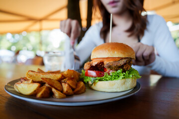 A woman is sitting at a restaurant table enjoying a delicious fried chicken burger with potato...