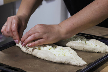 Woman folding dough into a boat shape, shredded suluguni cheese on the dough, preparing a Georgian cuisine dish, khachapuri. Close-up