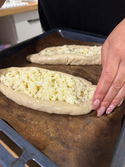 repared dough pieces on a baking tray, dough shaped into boats filled with shredded suluguni cheese, woman preparing a Georgian cuisine dish, khachapuri.