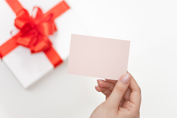 Fototapeta premium A blank note in a woman's hand against the background of a beautifully wrapped gift, top view, free space for text