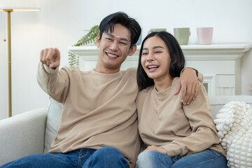 Fototapeta premium Happy couple laughing on the sofa and watching TV drama online