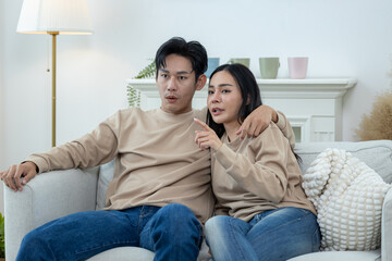Obraz premium Happy couple laughing on the sofa and watching TV drama online