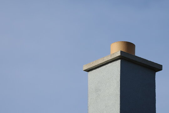 Minimalist close-up of a modern chimney structure with a concrete cap and cylinder against a pale blue sky. Architectural detail and design.