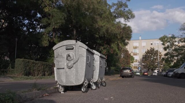Retro tinplate garbage cans with wheels on a street in the Csepel District, Budapest. An old post-communist residential area in Budapest, Hungary, with cars parked along the right side of the street.