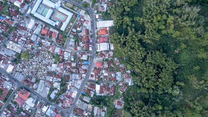 Naklejka premium A top-down aerial drone photo showing the border of Bajawa town, Indonesia. Dense urban housing with rusty tin roofs meets a lush green forest.