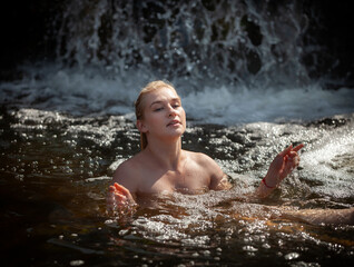 Fototapeta premium Blonde woman enjoying a refreshing swim in a natural waterfall