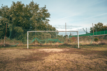 Old soccer goal on worn, uneven pitch with damaged grass and dusty ground, symbol of time and use.