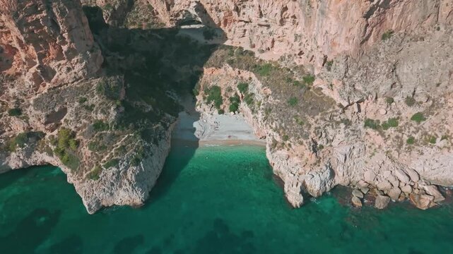 Top-down aerial view of Cala del Moraig cove and hidden beach surrounded by tall cliffs and crystal-clear turquoise water, Benitatxell, Spain.
