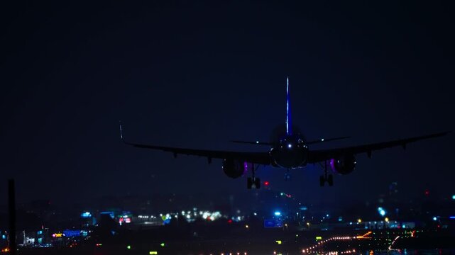Commercial aircraft approaching runway for landing at night with city lights and illuminated path