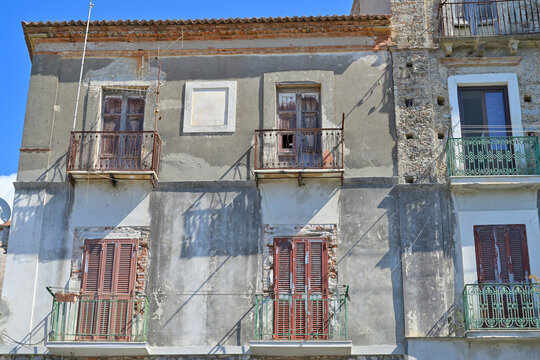 Old building facade showing weathered balconies and damaged windows in Scalea. Weathered building facade showcasing decay and neglect with damaged balconies and old shutters.