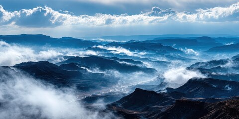 Naklejka premium A breathtaking view of rugged mountains shrouded in mist, under a dramatic sky filled with clouds, conveying a sense of vastness and tranquility.